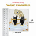A product image displaying a black statue of Lord Krishna's hands holding a golden flute and an ornate golden peacock feather with a blue gem detail, standing on a white base. A ruler on the left side and text on the right side indicate the product dimensions as 4.5 inches. The top of the image also displays