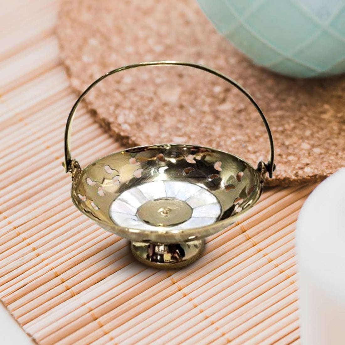 A handcrafted brass flower basket with mother of pearl inlays, placed on a bamboo mat.
