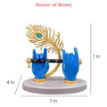 A blue Lord Krishna hand idol from House of Wemy, featuring a golden flute and a peacock feather, with indicated dimensions of 7 inches height, 4 inches width, and 7 inches depth.
