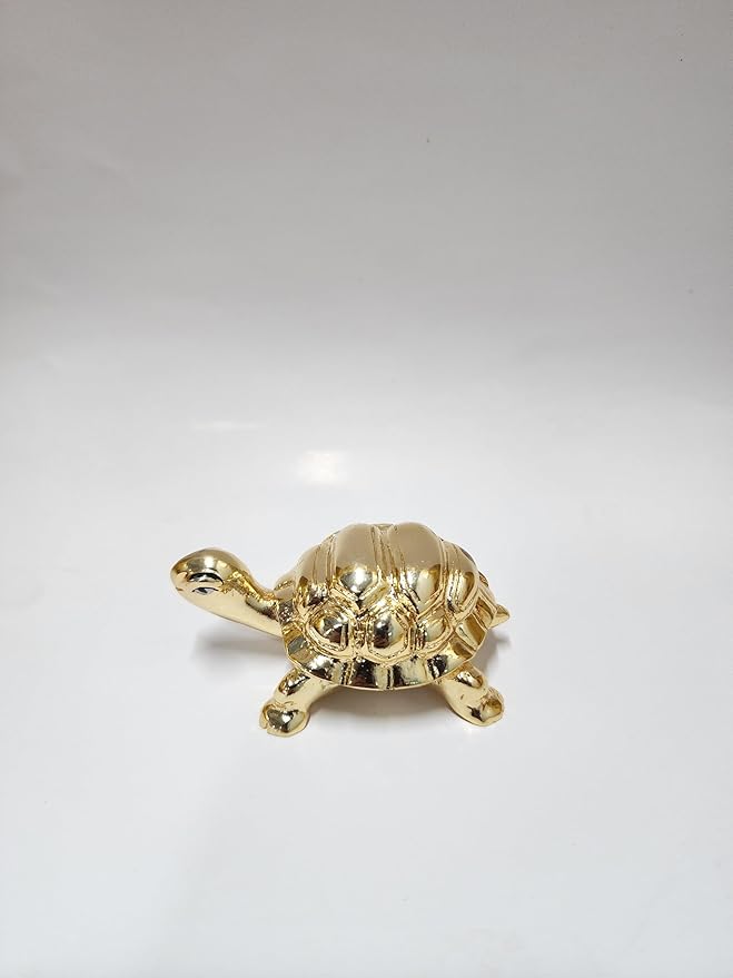 A small, gold-plated turtle figurine, a Feng Shui decorative item, is shown on a simple white surface. The turtle has a detailed shell and a shiny finish.