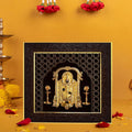 A gold-plated Lord Balaji photo frame with a dark, ornate border, featuring a detailed golden depiction of the deity, placed against a warm yellow-orange background with red flowers and petals, alongside traditional brass lamps.