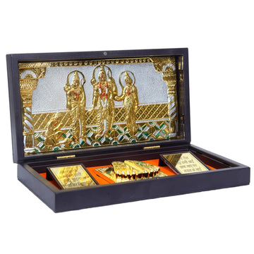 A dark brown, rectangular wooden box with a lid, open to reveal a gold-plated tableau of Ram Darbar inside. The tableau features Lord Rama, Goddess Sita, and Lord Lakshman standing, with Lord Hanuman kneeling before them, all intricately detailed and gold-plated against a silver and gold patterned background. The box also contains small, gold-plated items including a representation of Charan Paduka.