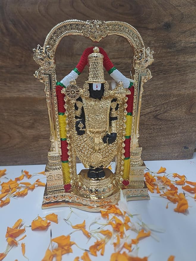 Gold-plated idol of Lord Tirupati Balaji (Venkateswara) standing within an ornate arch, set on a dark surface with a plate of traditional offerings and a red cloth in the foreground.