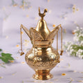 A brass etched handwork lota with intricate designs and a brass coconut, both with a golden shine, set against a floral backdrop.