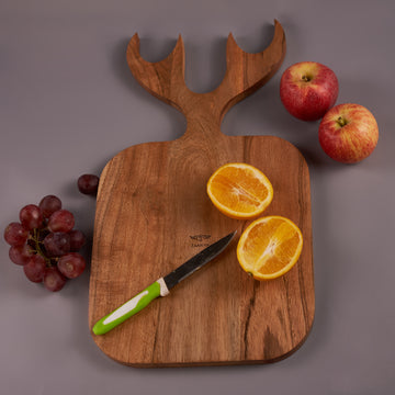 A wooden chopping board with a reindeer shape at the top, displayed with a knife and sliced fruits on it, against a grey background.