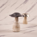 A silver mushroom-shaped decorative metal piece with an engraved pattern, displayed on a marble surface.