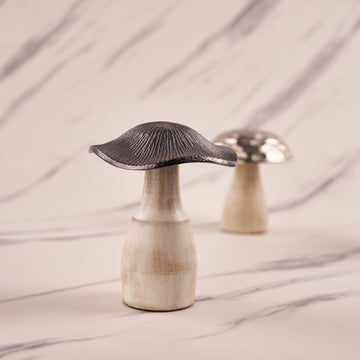 A silver mushroom-shaped decorative metal piece with an engraved pattern, displayed on a marble surface.