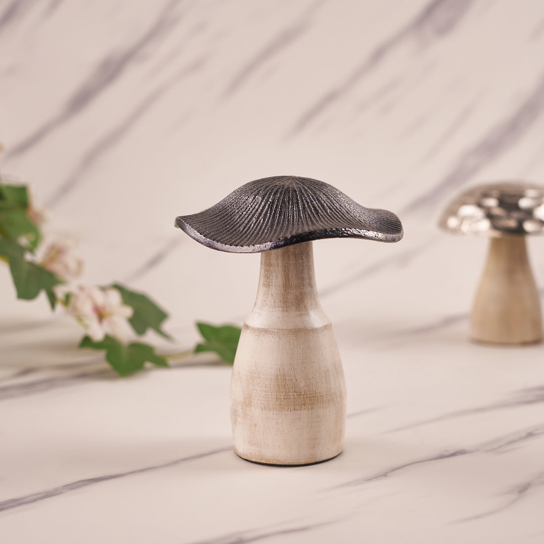 A silver mushroom-shaped decorative metal piece with an engraved pattern, displayed on a marble surface.