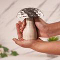 A decorative mushroom with a silver hammered pattern on the top cap carring with hands