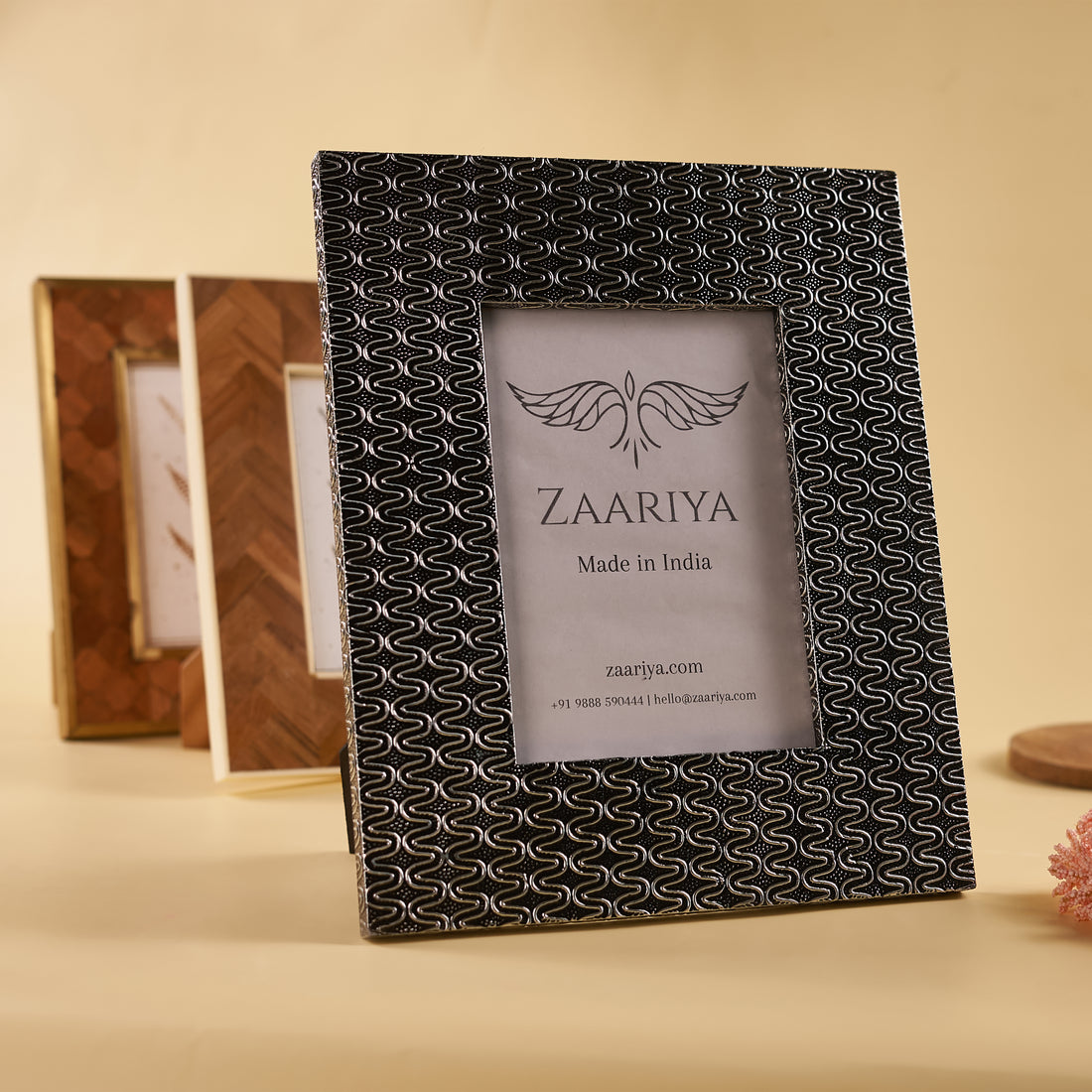 A wooden silver photo frame with a patterned design around the border, placed on a flat surface with a decorative item to the side.