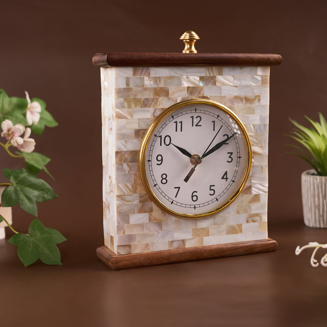 A Mother of Pearl table clock with a wooden frame, featuring a white clock face with black numerals, set against a brown background.