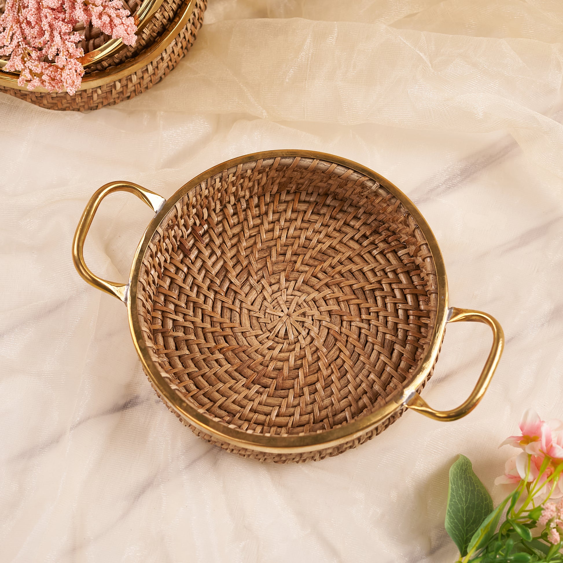 A small round rattan tray with handles, displayed on a neutral background, used for serving or organizing small items.
