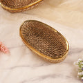 A long oval rattan basket with a beige color and a gold-colored rim, displayed on a soft, light background accompanied by small flowers.