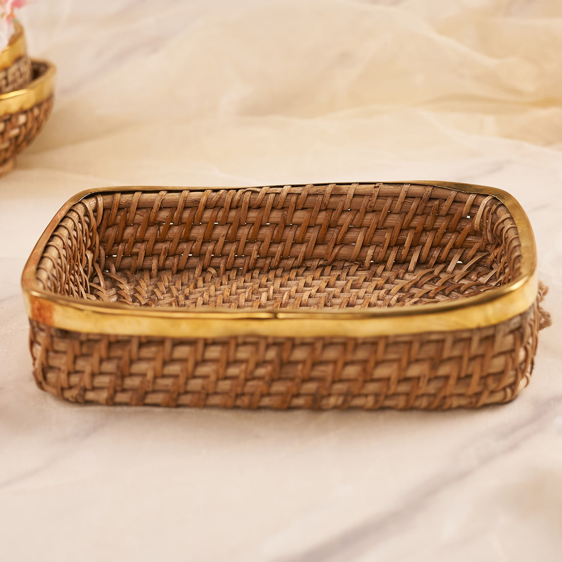 A rectangular rattan tray displayed on a neutral background, accompanied by fruits and flowers.