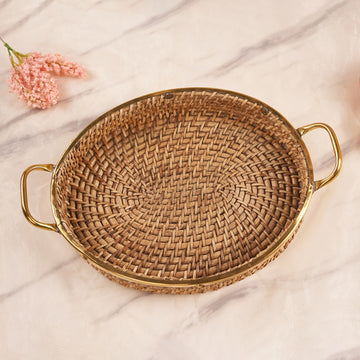 An oval-shaped rattan tray with handles, featuring a beige color and a finely woven design, displayed on a marble surface with a pink flower in the corner.