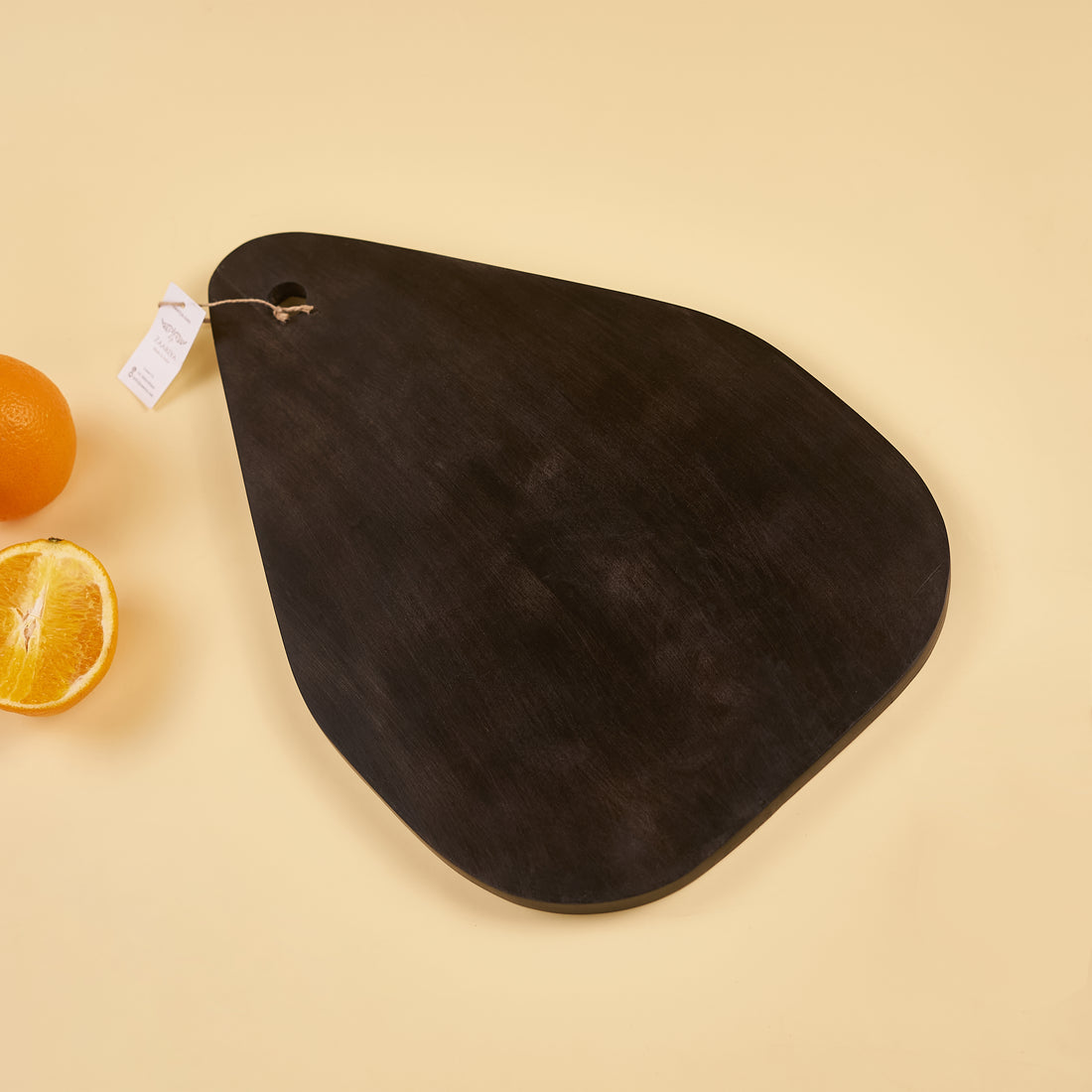 A black oval wooden platter with a tag attached to it, displaying an apple and orange on its surface, presented against a neutral background.