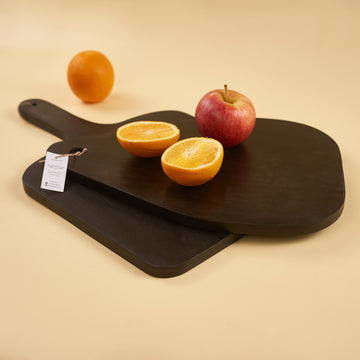 A black oval wooden platter with a tag attached to it, displaying an apple and orange on its surface, presented against a neutral background.