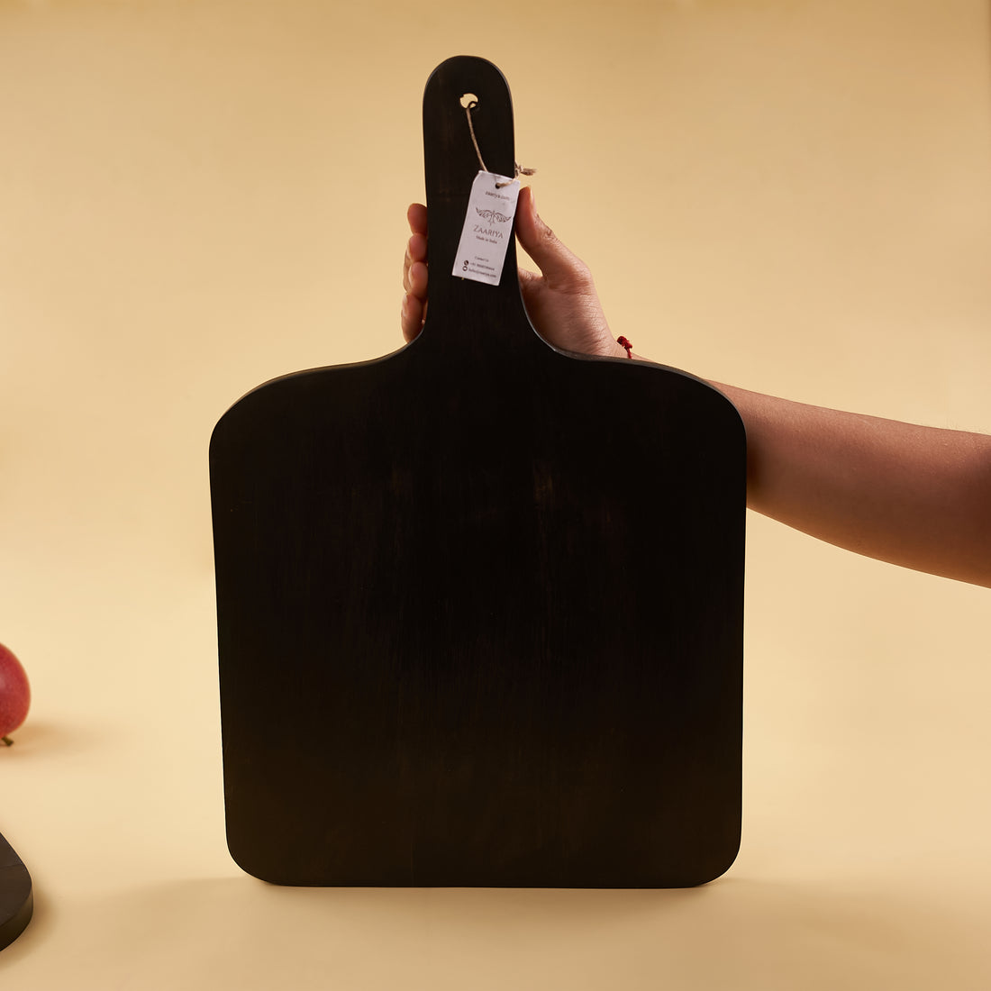 A black wooden platter with a handle, displaying a halved orange and a whole apple on a plain background.