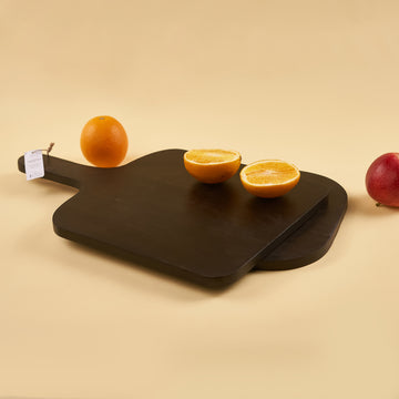 A black wooden platter with a handle, displaying a halved orange and a whole apple on a plain background.