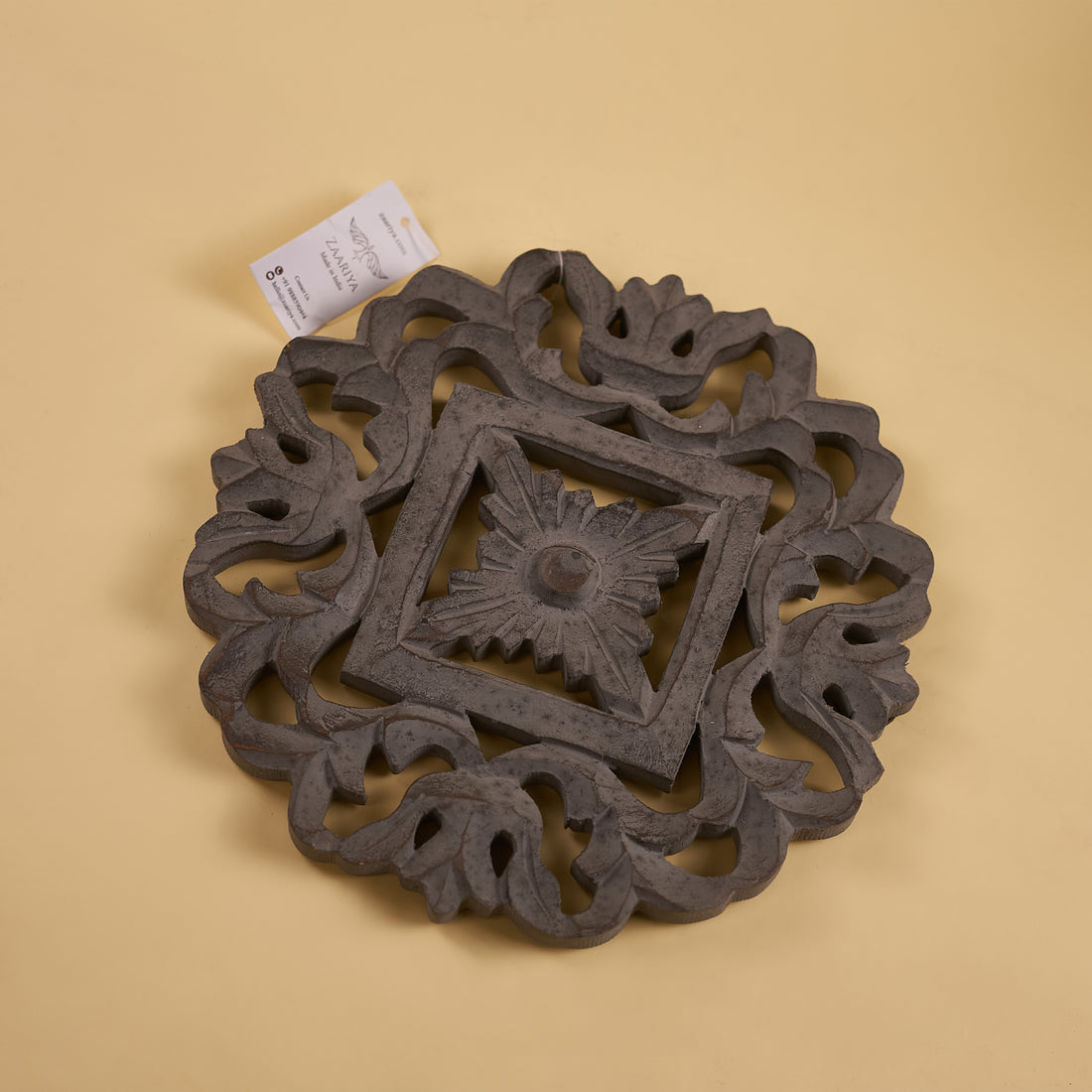A wooden carved trivet with a geometric pattern in a grey finish.