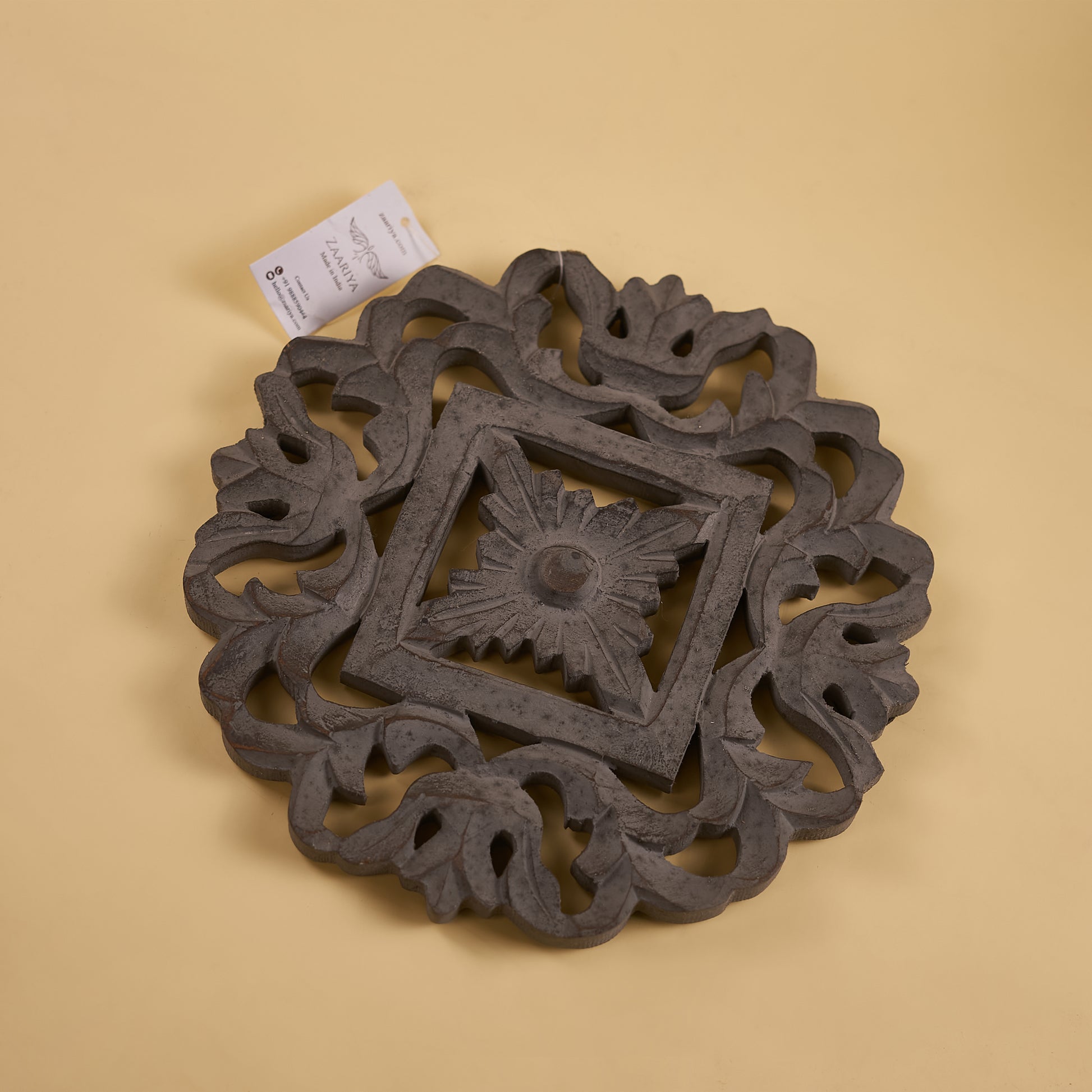 A wooden carved trivet with a geometric pattern in a grey finish.