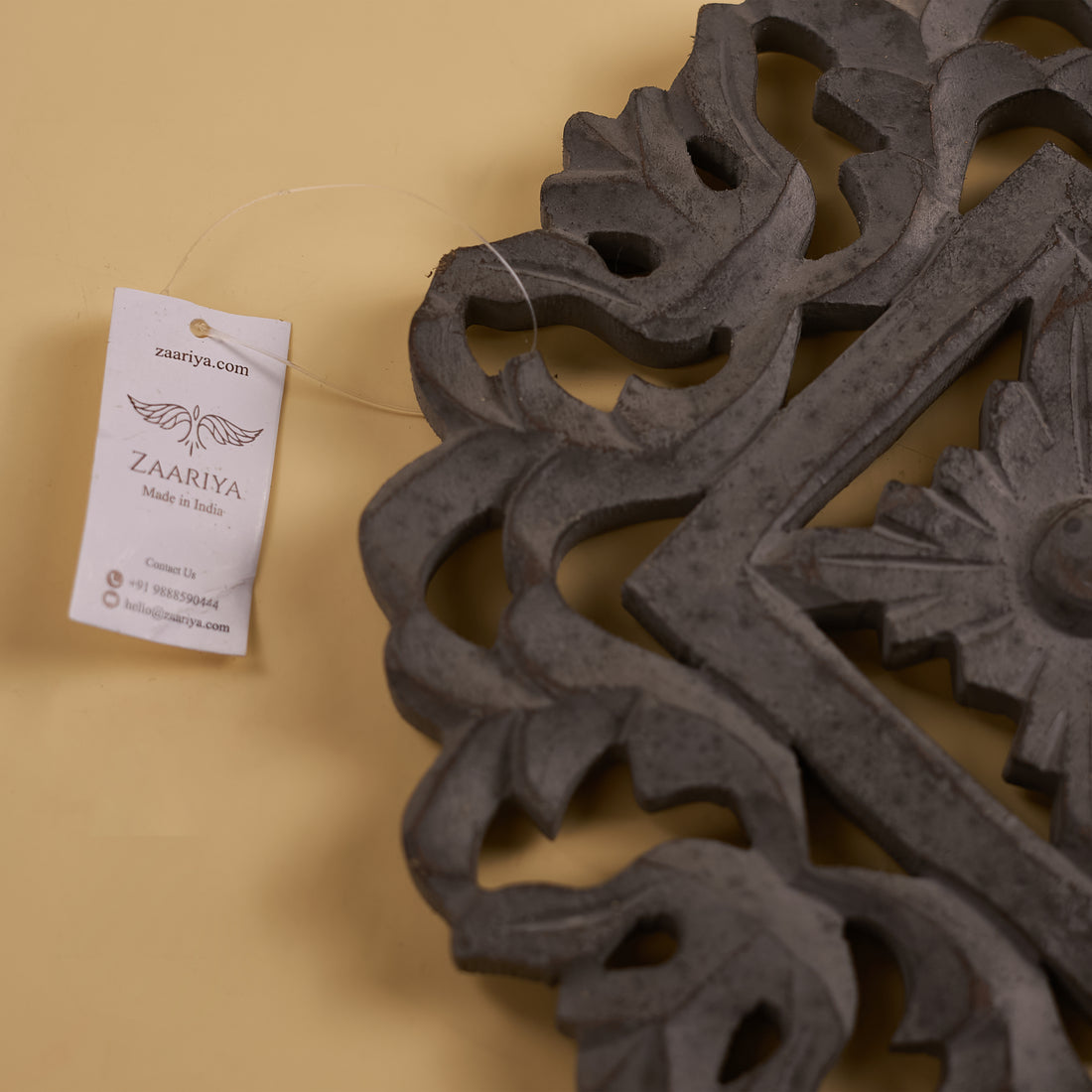 A wooden carved trivet with a geometric pattern in a grey finish.