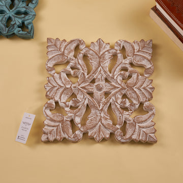A wooden carved trivet with an antique white finish, featuring intricate floral patterns, displayed on a yellow background.