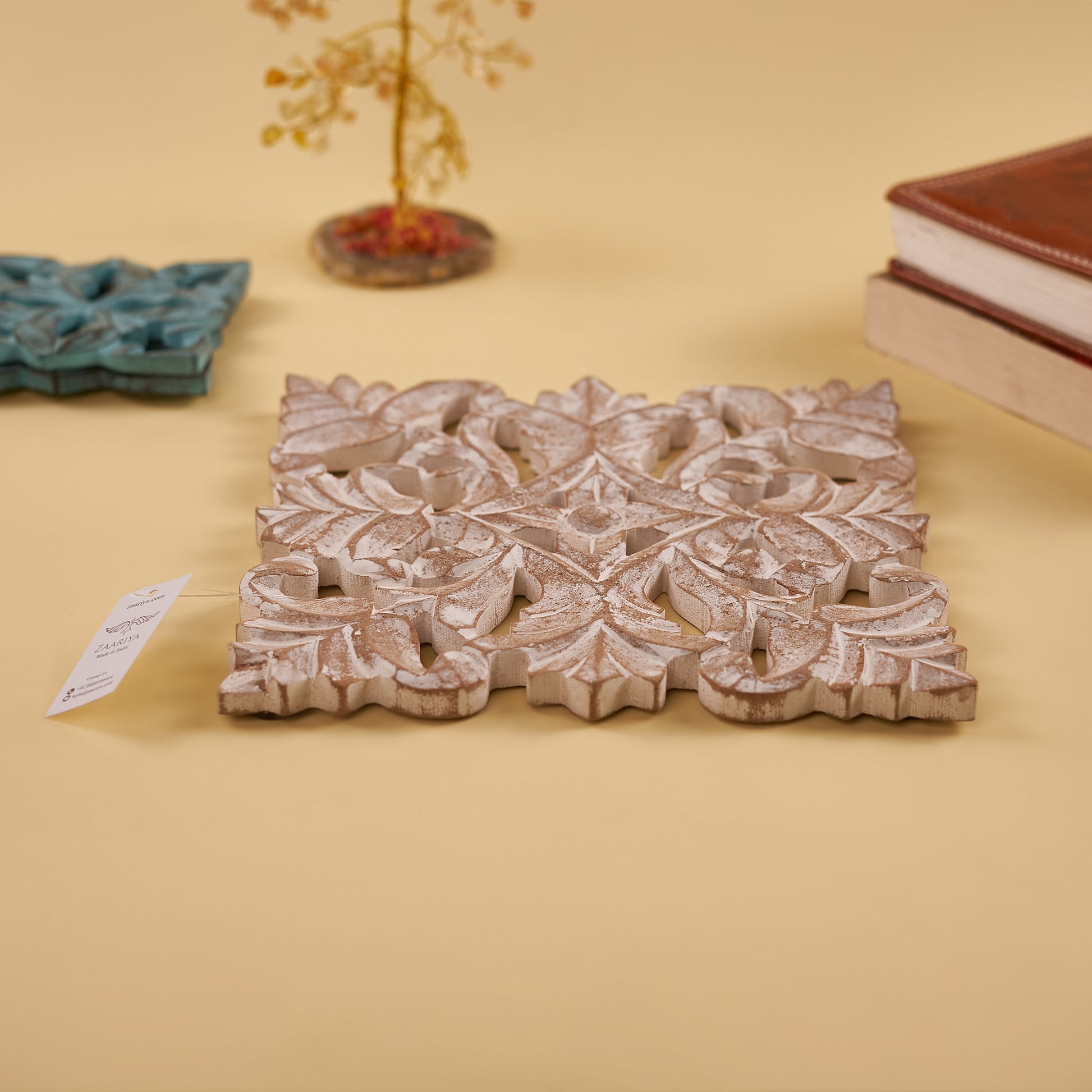 A wooden carved trivet with an antique white finish with green trivet set behind it