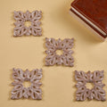 A set of four white wooden coasters with carved leaf patterns, displayed on a yellow background.