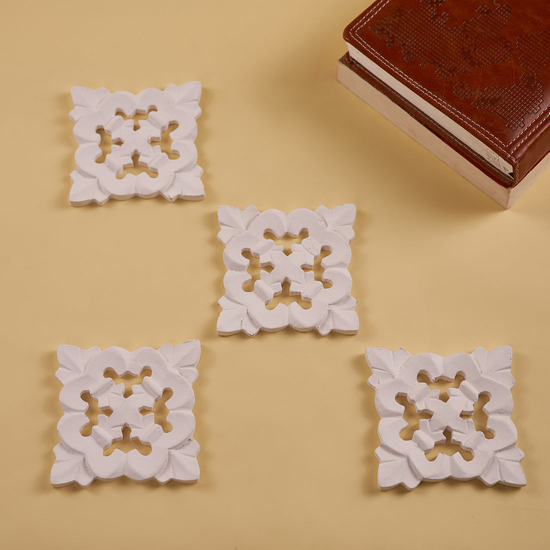 A set of four white wooden coasters with a floral pattern, displayed on a yellow surface.