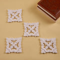 A set of four white wooden coasters with a floral pattern, displayed on a yellow surface.
