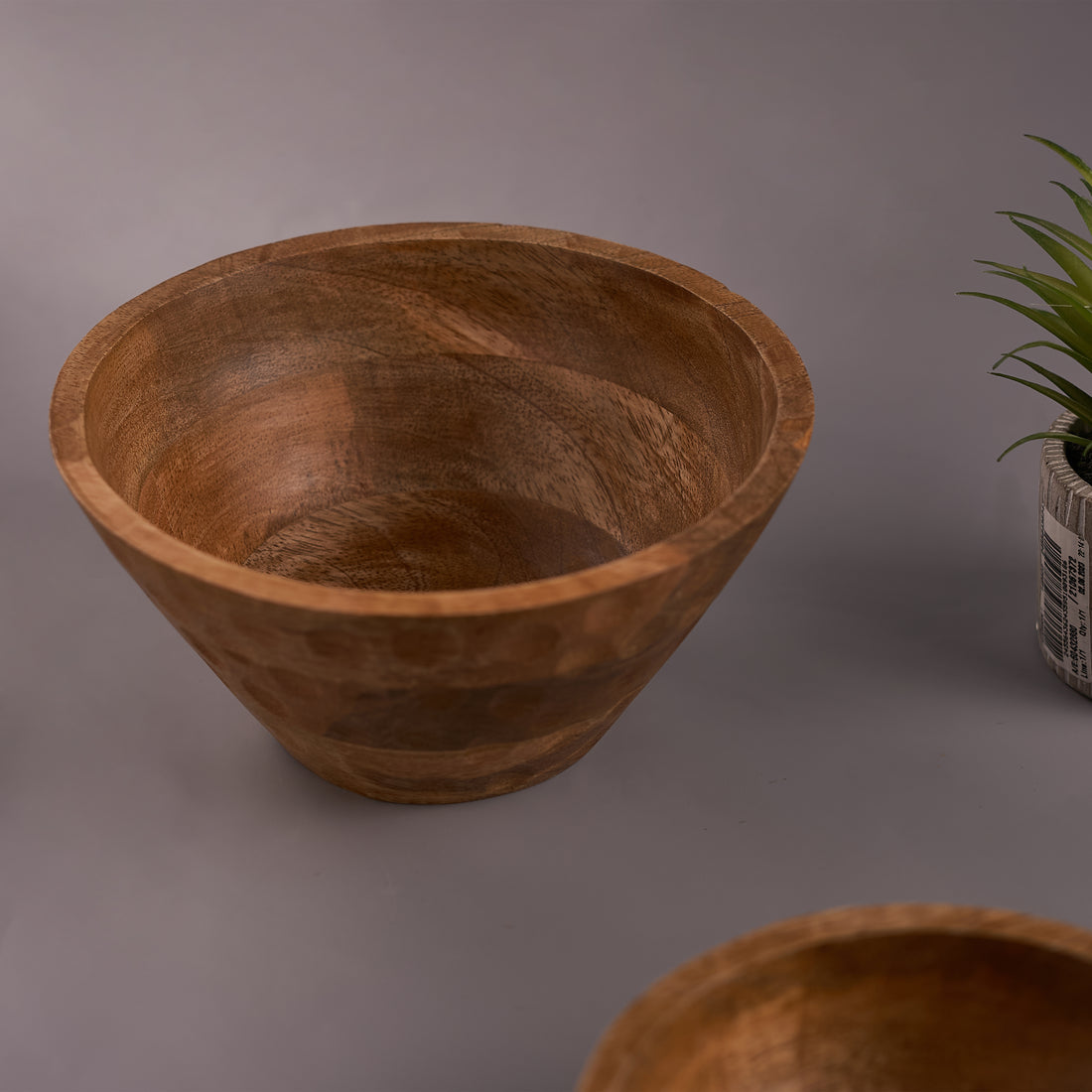 A rustic mango wood hammered bowl on a grey background, showcasing its unique textured surface and round shape.