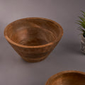 A rustic mango wood hammered bowl on a grey background, showcasing its unique textured surface and round shape.