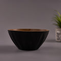 A black Mango Wood bowl with a walnut finish on a gray background, with a plant decoration in the corner.