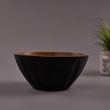 A black Mango Wood bowl with a walnut finish on a gray background, with a plant decoration in the corner.