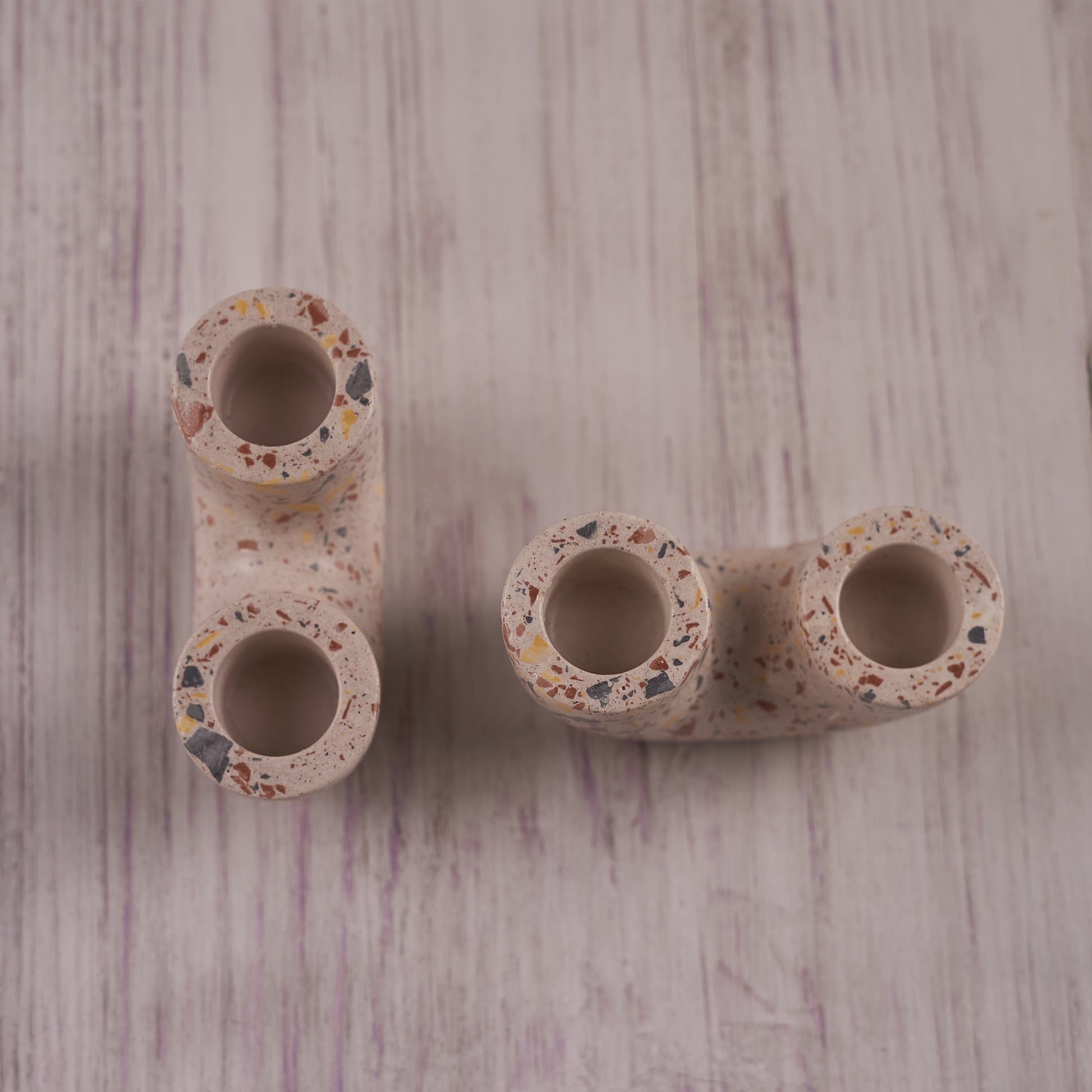 A U-shaped, terrazzo-style Ceramic Curve Candle Holder Set of 2 is displayed on a light wooden background. The speckled design features small, colorful flecks, and each holder has two openings for taper candles.