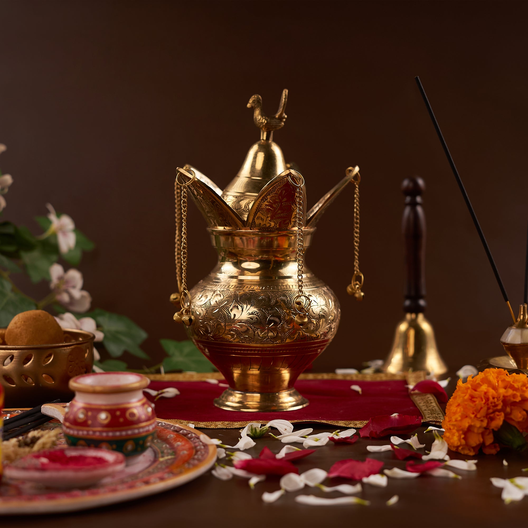 Brass lota on the red chariot with pooja thali, flowers and bell around it