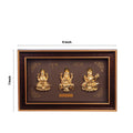 A rectangular brown and gold framed art piece, 7 by 11 inches, featuring three golden, embossed Hindu deities: Goddess Lakshmi on the left, Lord Ganesha in the center, and Goddess Saraswati on the right. Above the deities, the words