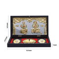 A black framed gift box containing golden idols of Goddess Lakshmi and Lord Ganesha, a pair of golden Lakshmi Charan Padukas (footprints), and two golden coins inscribed with the word