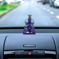 A blue and gold Ganesha idol placed on the dashboard of a car, with the road visible through the windshield in the background.