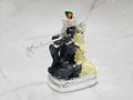 A silver-plated idol of Radha Krishna on a marble surface. Krishna is depicted in dark stone, playing a silver flute, while Radha in light stone sits beside him, adorned with intricate details and a peacock feather on Krishna's crown.