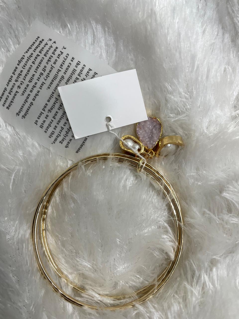 A set of two gold-colored brass metal bangle bracelets with semi-precious stone accents, displayed on a white furry surface.