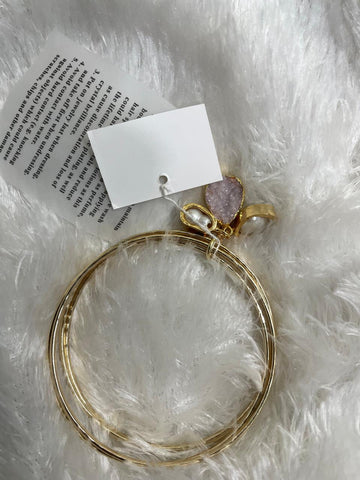 A set of two gold-colored brass metal bangle bracelets with semi-precious stone accents, displayed on a white furry surface.