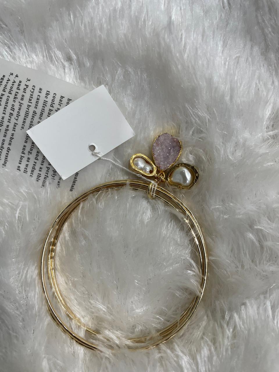 A set of two gold-colored brass metal bangle bracelets with semi-precious stone accents, displayed on a white furry surface.