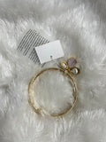 A gold-toned brass metal bangle set is displayed on a soft, white furry surface. The bangles are adorned with a decorative butterfly-shaped clasp that has a mother-of-pearl or iridescent stone and a pearl. A white tag is attached to the bangles.