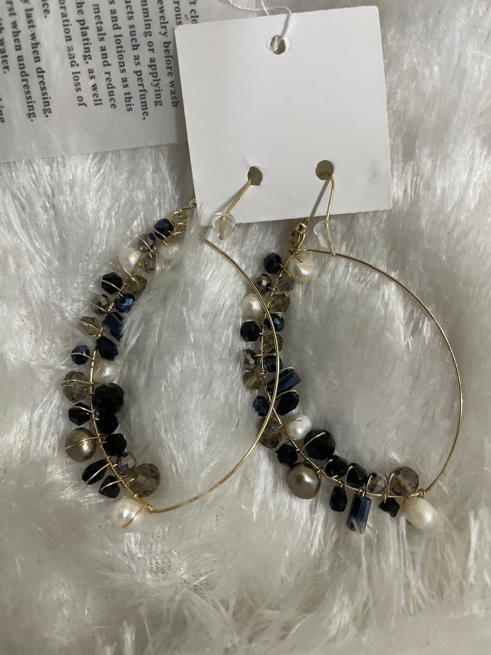 A pair of black and grey finish crystal bead wrapped earrings displayed on a white fuzzy surface, with a cardboard tag attached to the top.