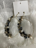 A pair of large, gold-toned hoop earrings are shown on a light-colored, fluffy background. One side of each hoop is wrapped with a cluster of various beads, including small white pearls and faceted Crystal Bead Wrapped Earrings in Black & Grey in different shapes and sizes.