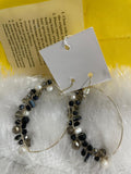 A pair of large, gold-toned hoop earrings are displayed on a soft, light-colored background. The earrings are embellished with a cluster of beads, including small white pearls and faceted Crystal Bead Wrapped Earrings in Black & Grey, wrapped along one side of each hoop.