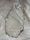 A brass long chain necklace with Swarovski pearl beads on a white furry surface.