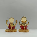 Two golden idols of Hindu deities Ganesha and Lakshmi sitting side-by-side on a light background.